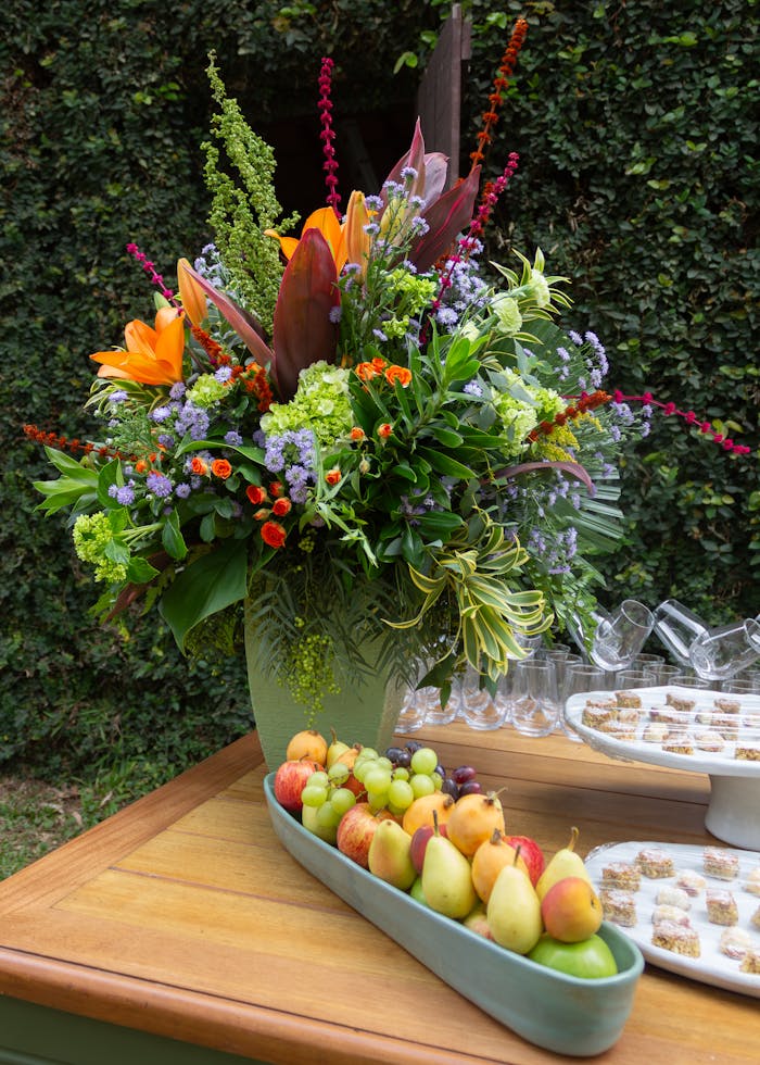 gallery-3 A colorful floral bouquet with fresh fruits on a wooden table outdoors.