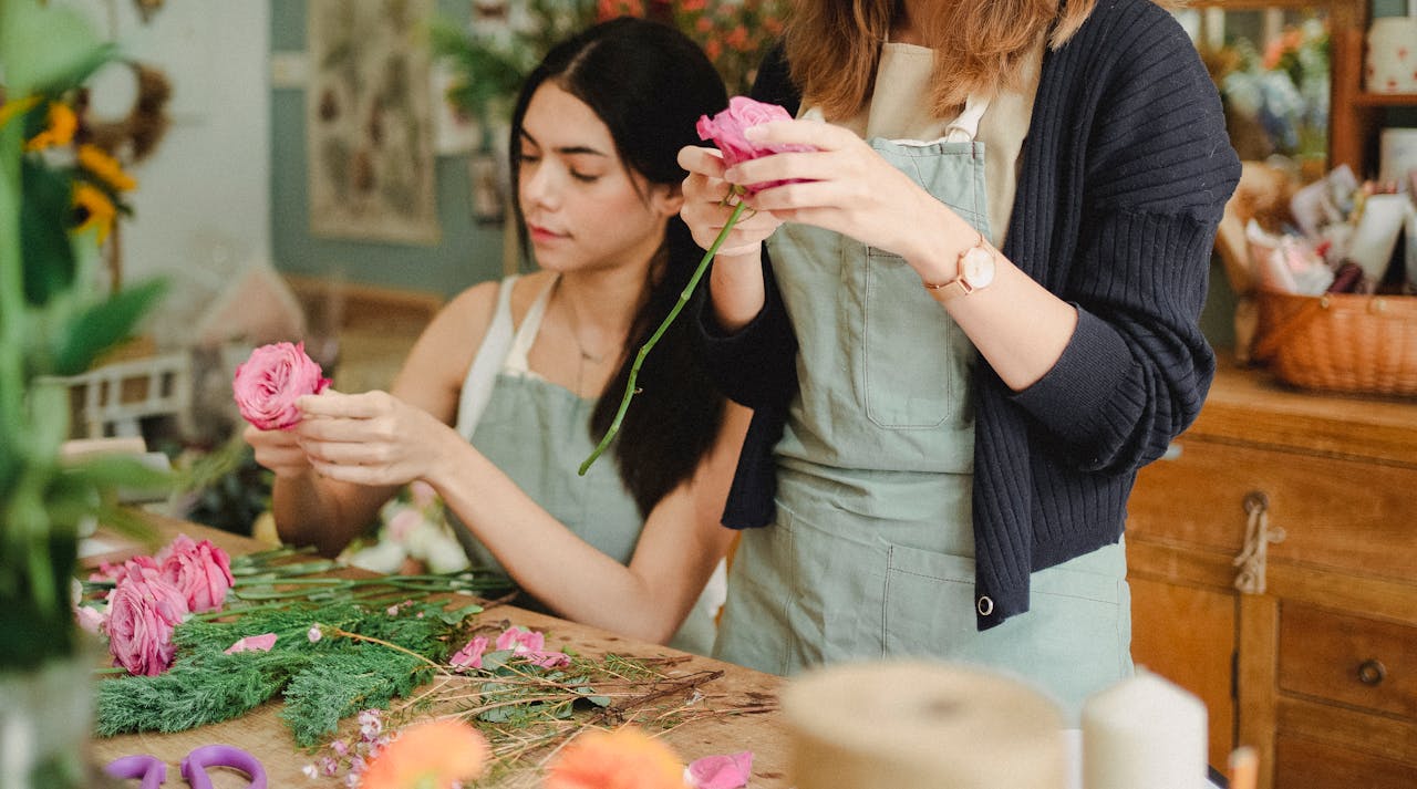 services-img Positive young female florists wearing aprons removing leaves from flower stems before arranging bouquet in modern floristry store