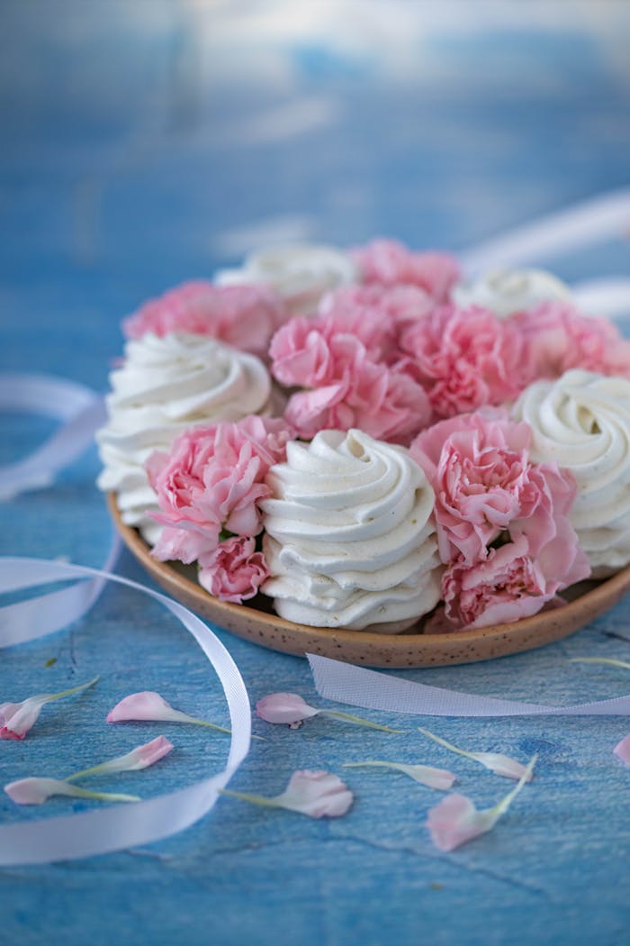 why-choose-us Arrangement of white sweet zephyr with tender pink flowers served on plate on blue table with scattered petals and ribbon